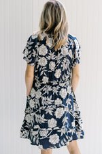 Back view of Model wearing a navy dress with a white floral pattern and short sleeves. 