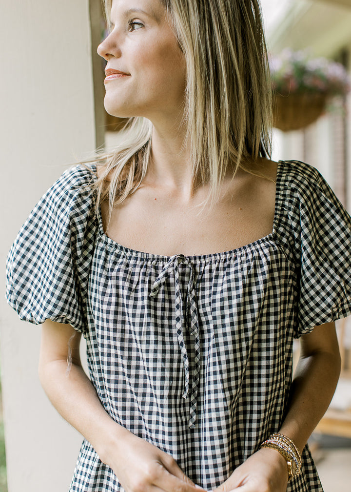 Close up of square neck with faux tie at neck and bubble short sleeves on a navy and cream gingham.