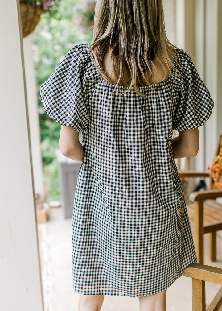 Back view of Model wearing a navy and cream gingham dress with square neck and bubble sleeves.