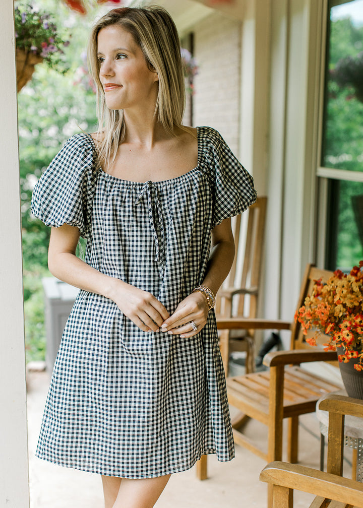 Model wearing a navy and cream gingham above the knee dress with square neck and short sleeves.