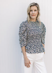 Model wearing a navy top with micro-floral print, elbow length sleeves and a ruffle neck. 