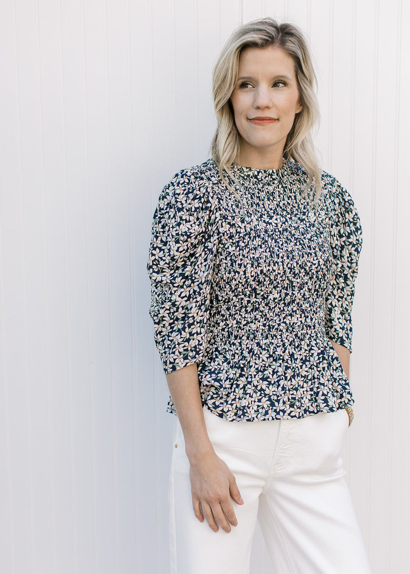 Model wearing a navy top with micro-floral print, elbow length sleeves and a ruffle neck. 