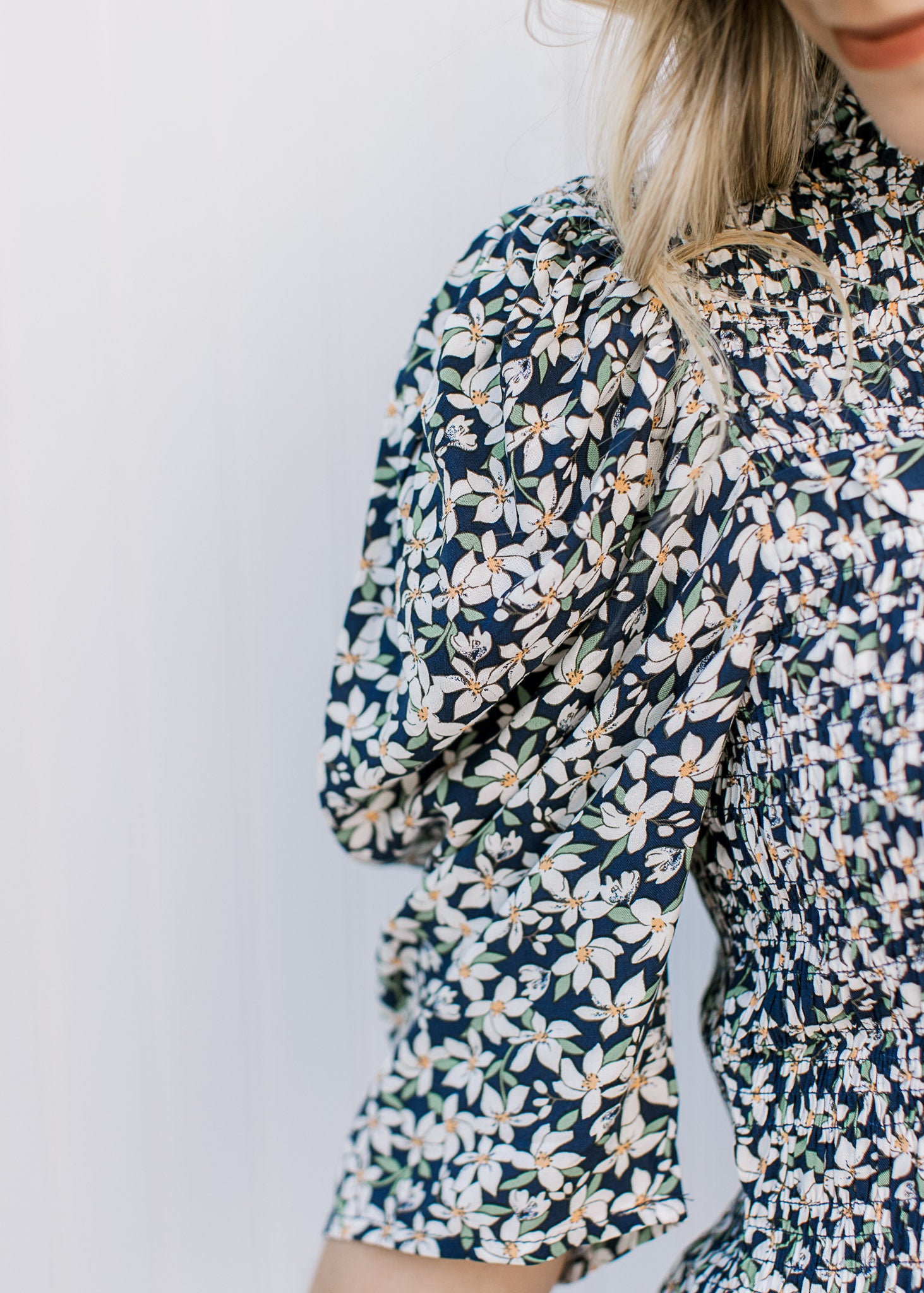 Close up of elbow length sleeves with pleated shoulder and smocked  bodice on a navy floral top.