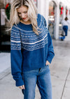 Model wearing jeans and a blue sweater with a cream pattern, long sleeves and a round neck.
