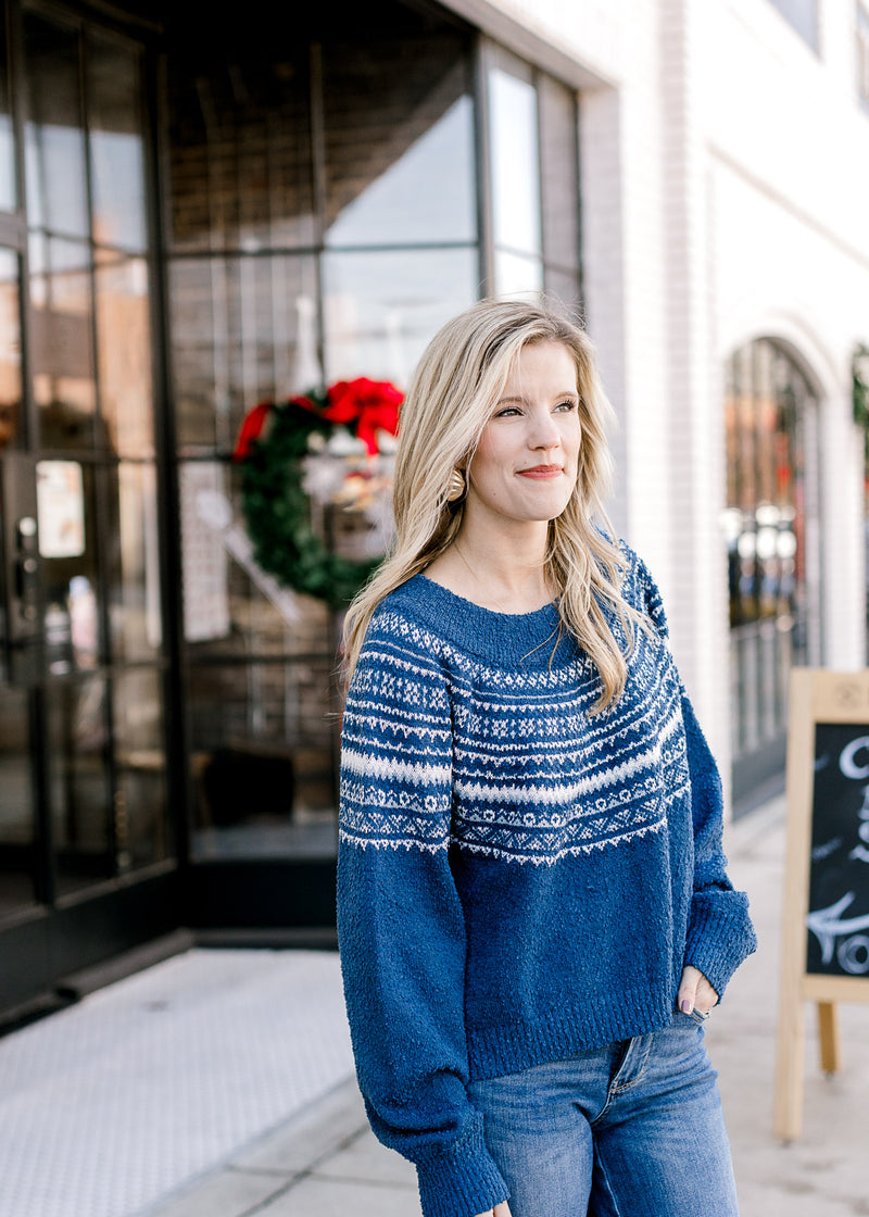 Model wearing a cobalt blue sweater with a cream fair isle pattern, long sleeves and a round neck.