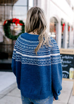 Back view of Model wearing a blue sweater with a cream pattern, long sleeves and a round neck.