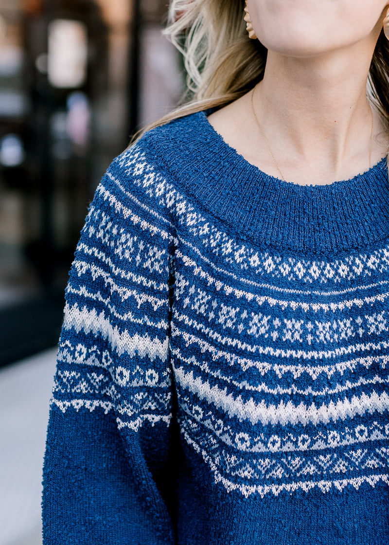 Close up of cream fair isle pattern on a cobalt blue sweater with long sleeves and a round neck.