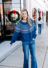 Model wearing a cobalt blue sweater with a cream pattern, long sleeves and a round neck.