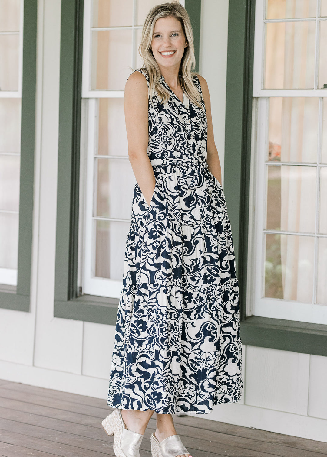 Model wearing wedges and a navy maxi with cream floral pattern, tie at waist and pockets. 