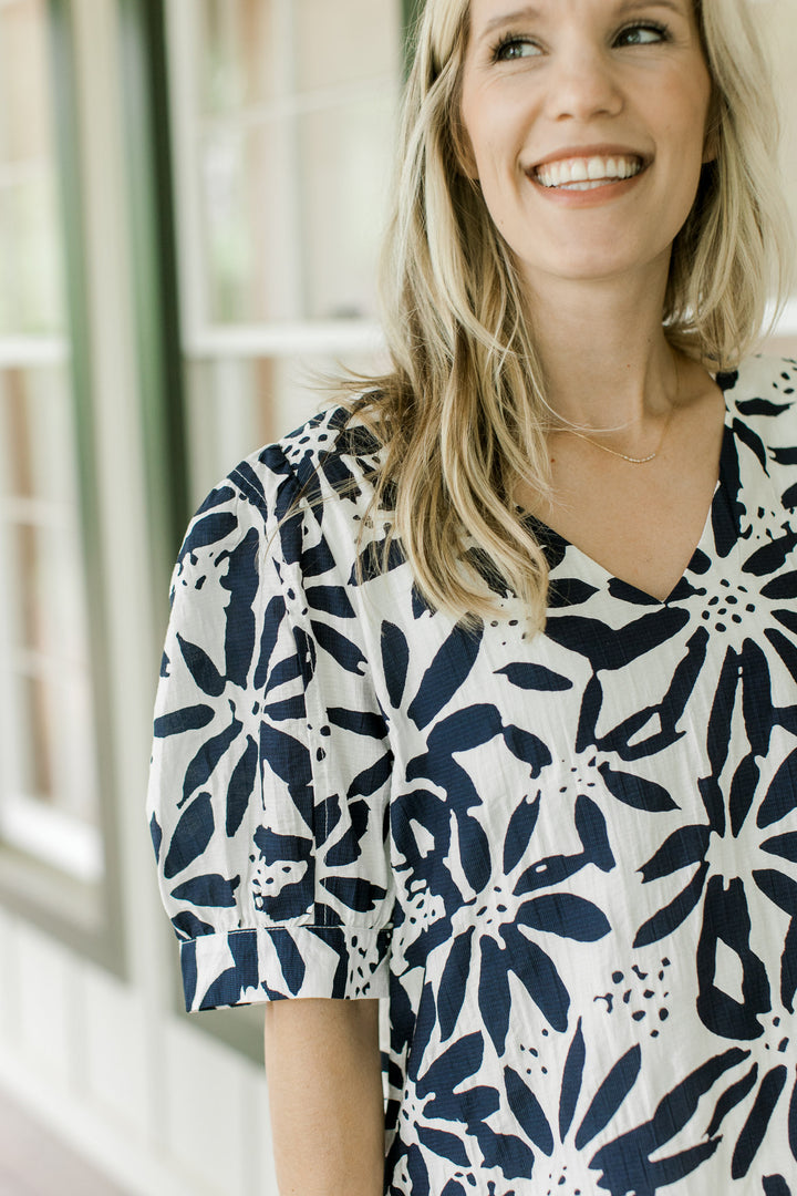 Close up of short puff sleeves and a v-neck on an off white dress with navy flowers. 