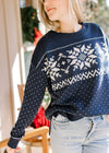 Model wearing a navy sweater with a  snowflake pattern, long sleeves and a vintage feel. 