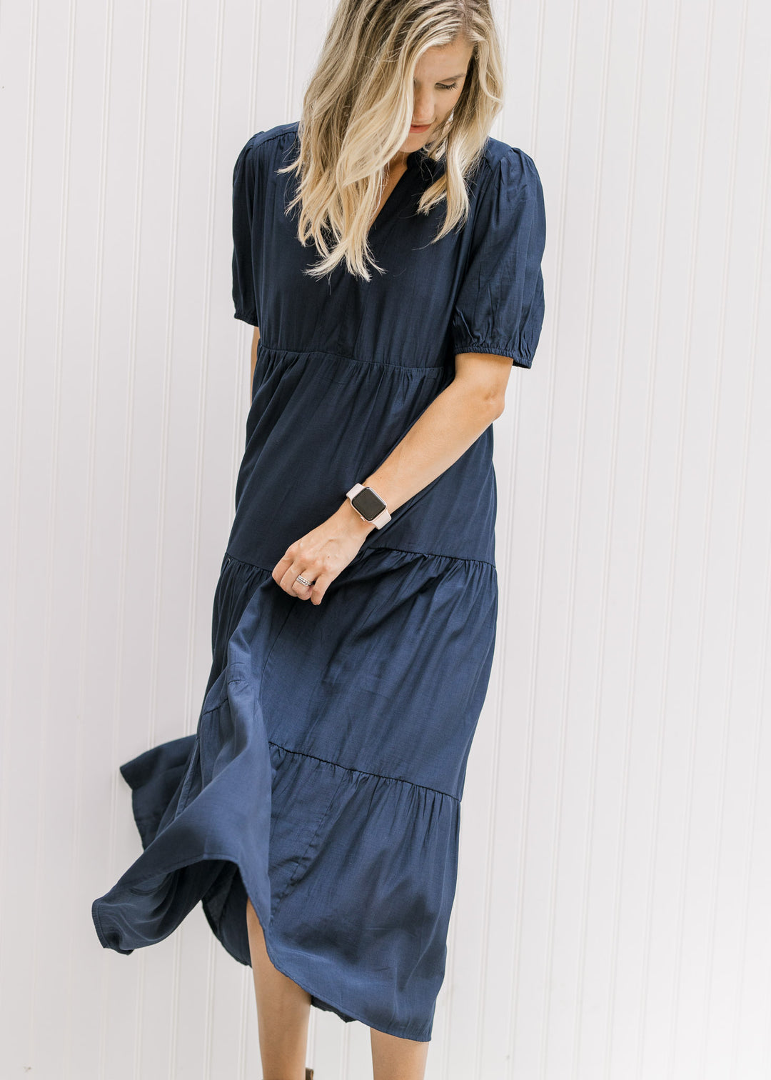 Model twirling in a tiered navy dress with a v-neck and bubble short sleeves.