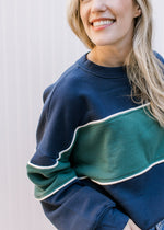 Model wearing a navy long sleeve,crew neck sweatshirt with a green strip in the middle. 