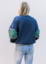 Back view of Model wearing a navy long sleeve sweatshirt with a green strip in the middle. 