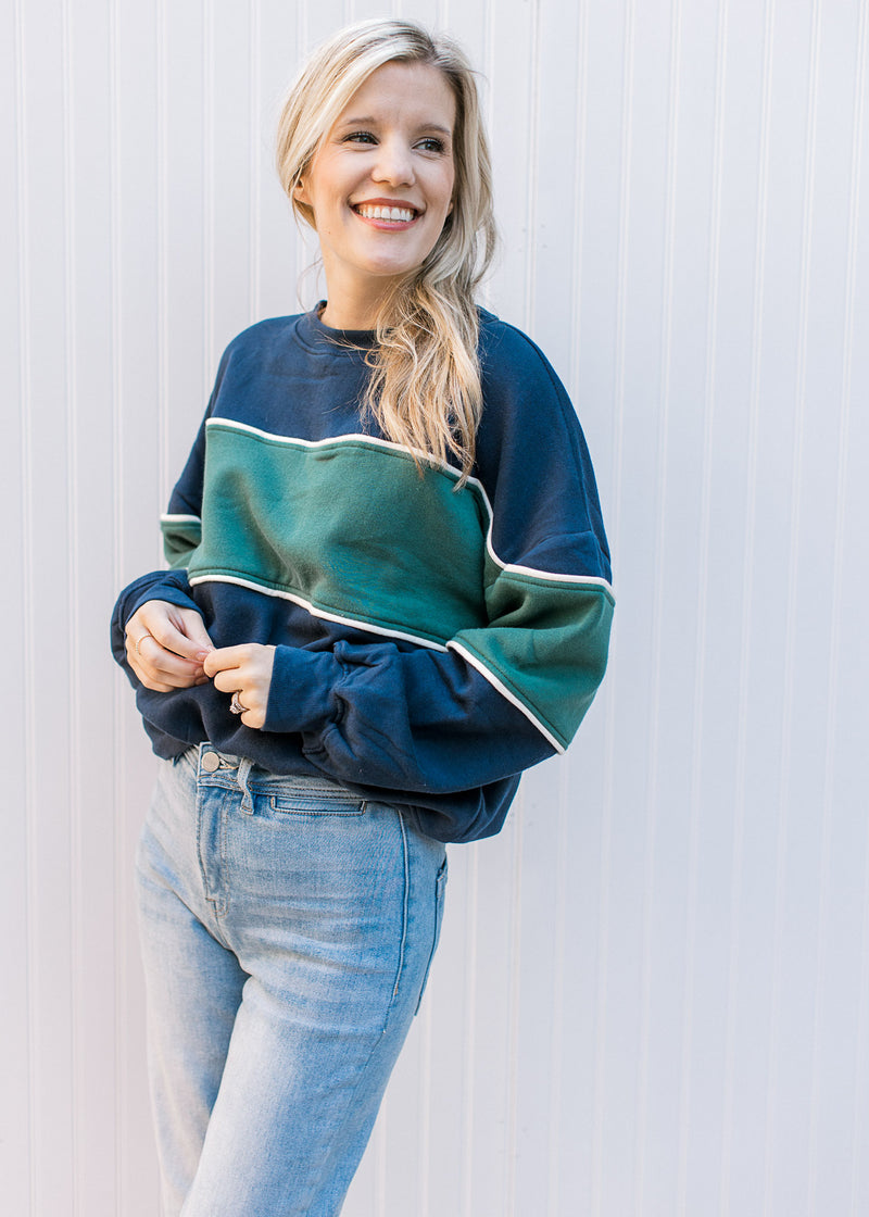 Model wearing jeans with a navy long sleeve,crew neck sweatshirt with a green strip in the middle. 