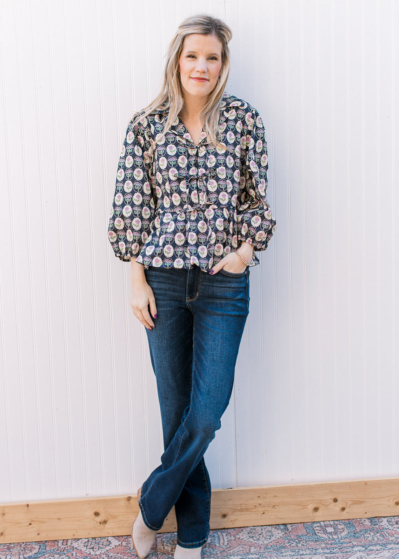 Model wearing jeans and a navy top with cream, pink and blue floral pattern and tie front closure