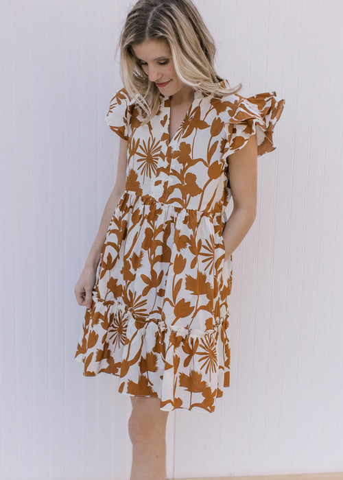 Model wearing a cream dress with rust floral pattern, ruffle short sleeves, v-neck and pockets. 
