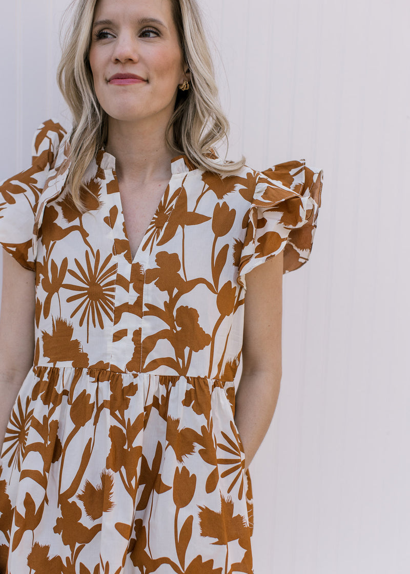 Close up of v-neck and ruffle short sleeves on a cream cotton dress with a rust floral pattern. 
