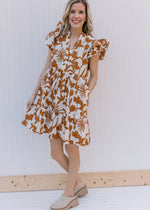 Model wearing mules and a cream dress with rust floral pattern, ruffle short sleeves and v-neck.