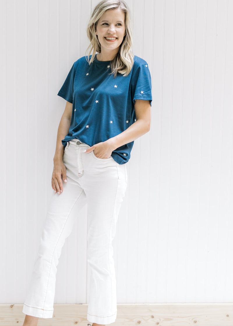 Model wearing white jeans with a navy top with cream embroidered stars and short sleeves. 