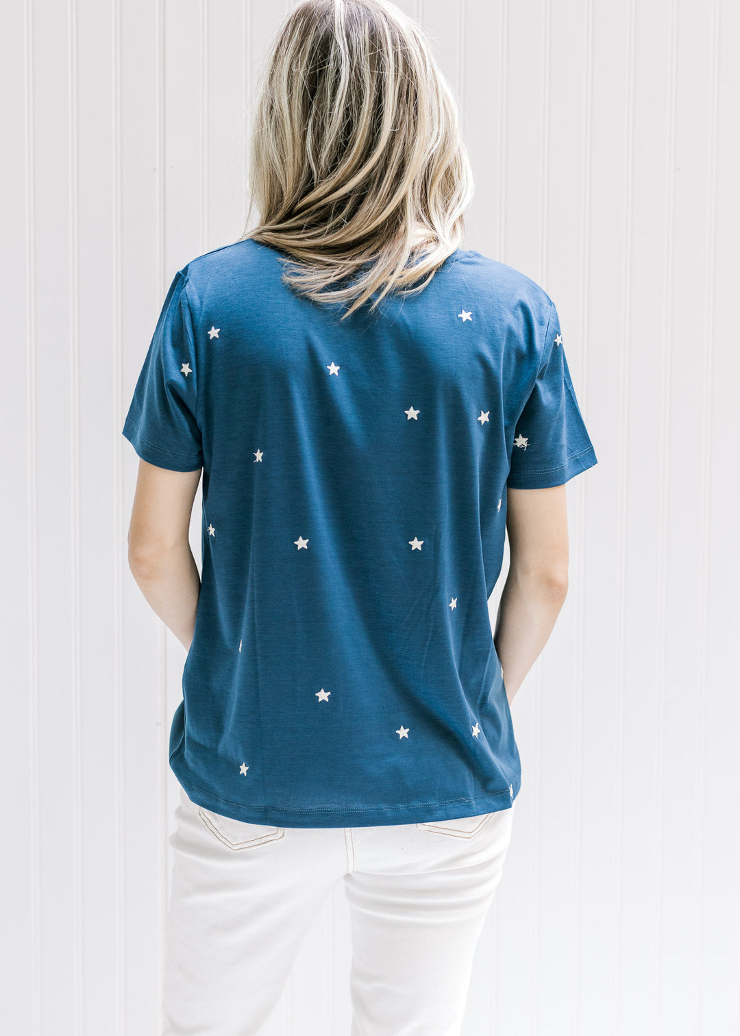 Back view of Model wearing a navy top with cream embroidered stars a round neck and short sleeves. 
