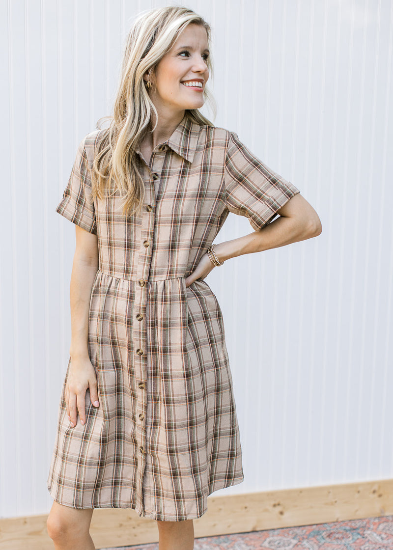 Model wearing a taupe plaid dress with button front, collar and short sleeves with cuff. 