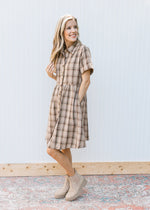 Model wearing booties with a taupe plaid dress with button front, collar and short sleeves. 