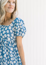 Model wearing a blue dress with white daisies, a square neck and bubble short sleeves.