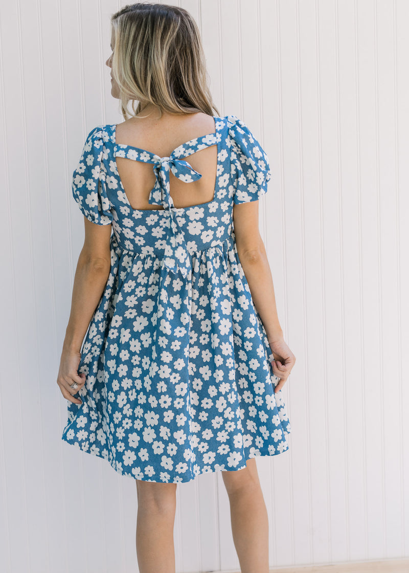 Back view of a model in a blue dress with white daisies, bubble short sleeves and a tie closure. 