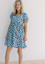 Model wearing a blue above the knee dress with white daisies, a square neck and bubble short sleeves
