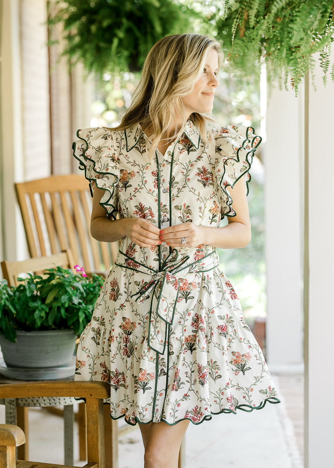 Model wearing a cream above the knee dress with floral print, button front and ruffle cap sleeves.