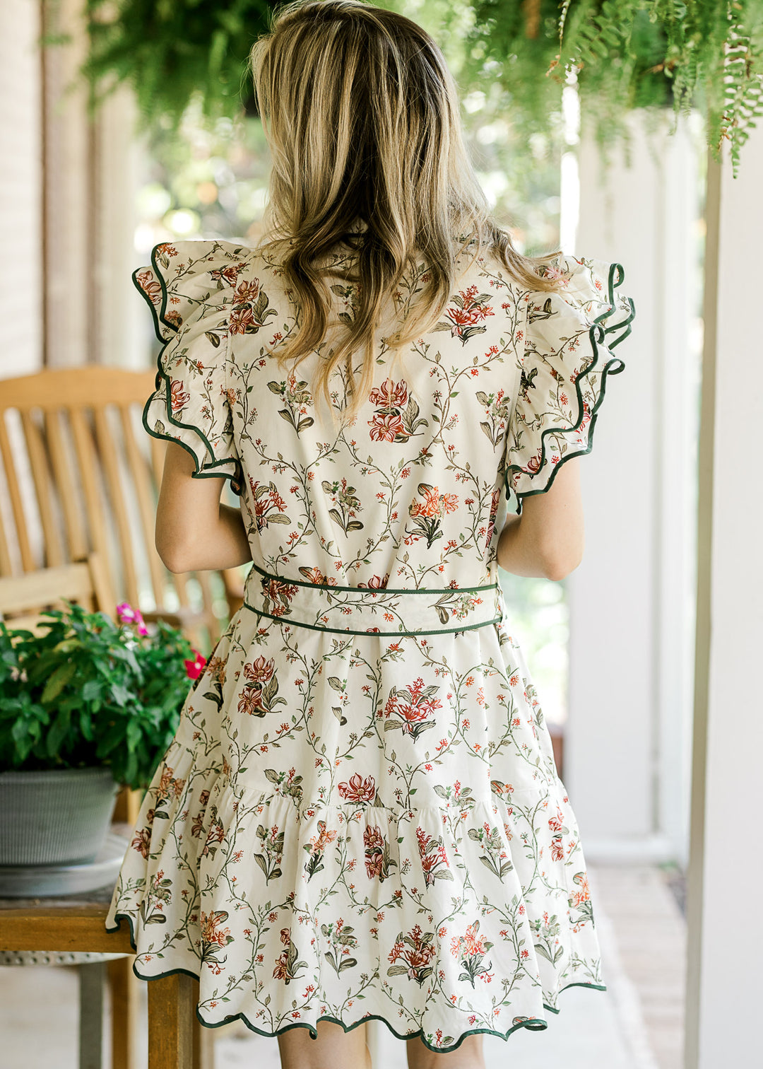 Back view of Model wearing a cream dress with floral print, button front and ruffle cap sleeves.