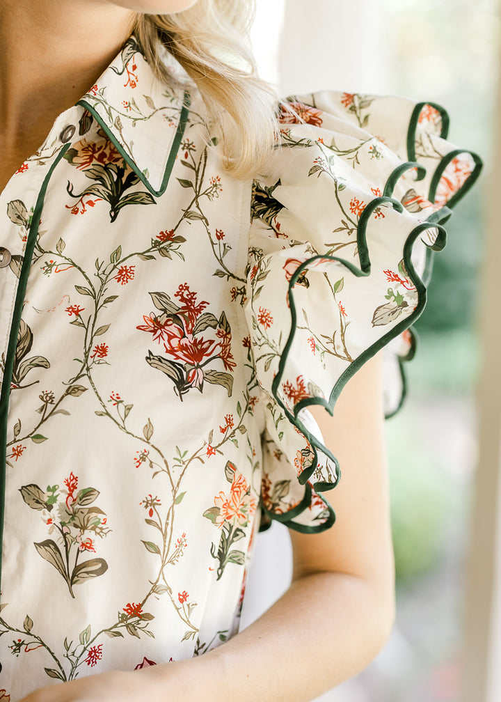 Close up of layered ruffle cap sleeve on a button up above the knee cream dress with floral print.