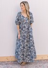 Model wearing a gray, v-neck maxi with navy floral, short puff sleeves and an elastic waist. 