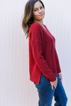 Side view of Model wearing a wine, waffle knit, v-neck sweater with long sleeves and  split sides.