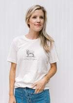 Model wearing an off white short sleeve tee with “and now I’m Found” and a sheep in black.