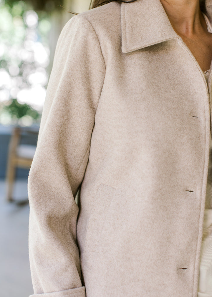Close up of flap collar, long sleeves and buttons on an oatmeal jacket with side pockets. 