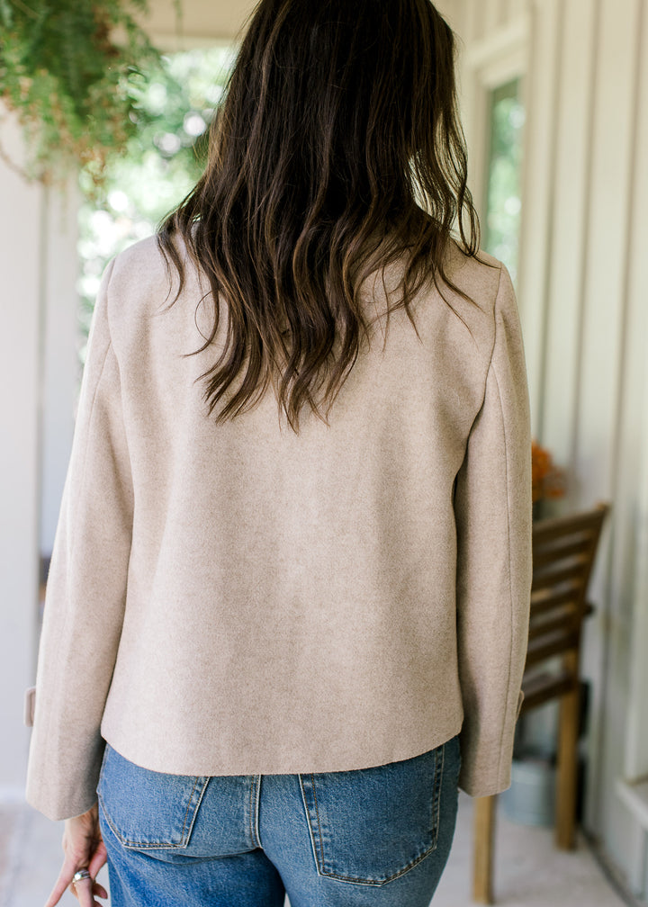 Back view of Model wearing a long sleeve oatmeal jacket with flap collar and side slit pockets.