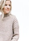 Model wearing a ribbed oatmeal sweater with a mock neckline, long sleeves and polyester material. 