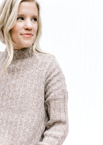 Model wearing a ribbed oatmeal sweater with a mock neckline, long sleeves and polyester material. 