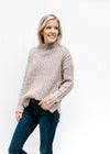 Model wearing jeans and a ribbed oatmeal sweater with a mock neckline and long sleeves. 