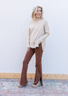 Model wearing an oatmeal colored sweater with split sides, long sleeve and cut out design.