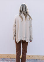 Back view of Model wearing an oatmeal sweater with mock neck, long sleeve and cut out design.