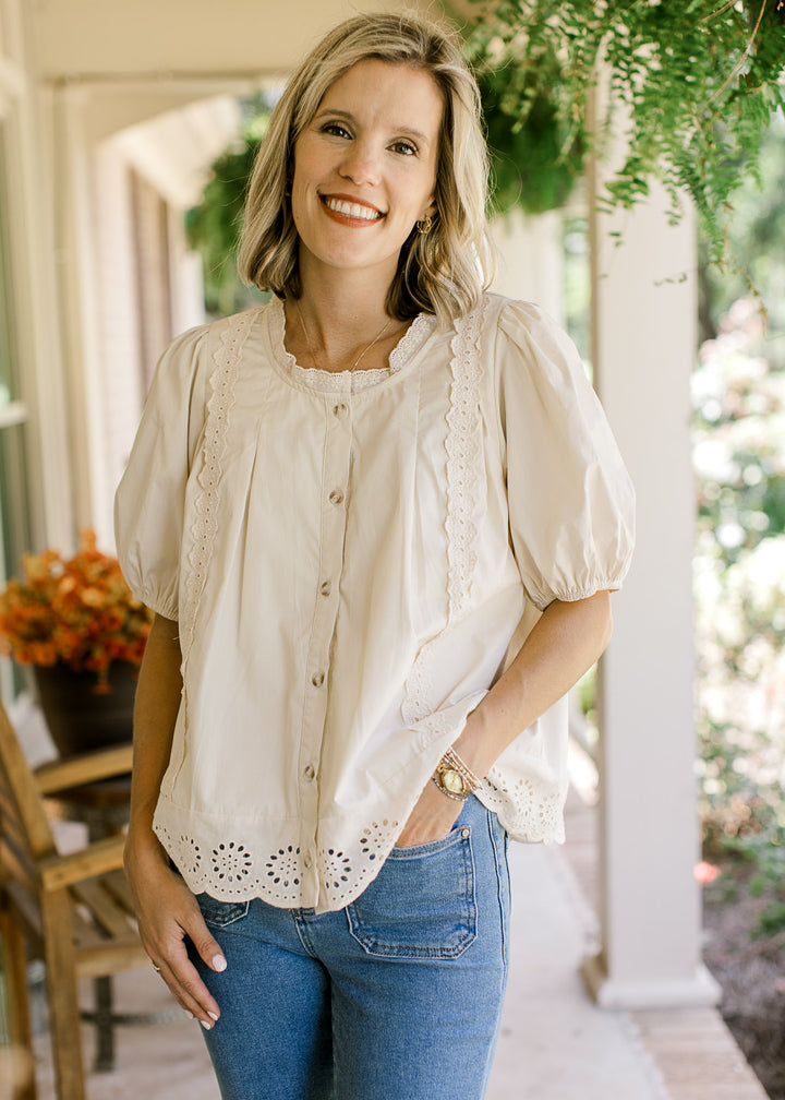 Model wearing a button up oatmeal top with lace detail, short sleeves and eyelet scalloped hem.