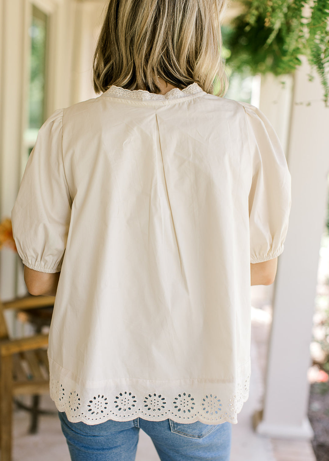 Back view of Model wearing an oatmeal top with short sleeves and scalloped hem with eyelets.