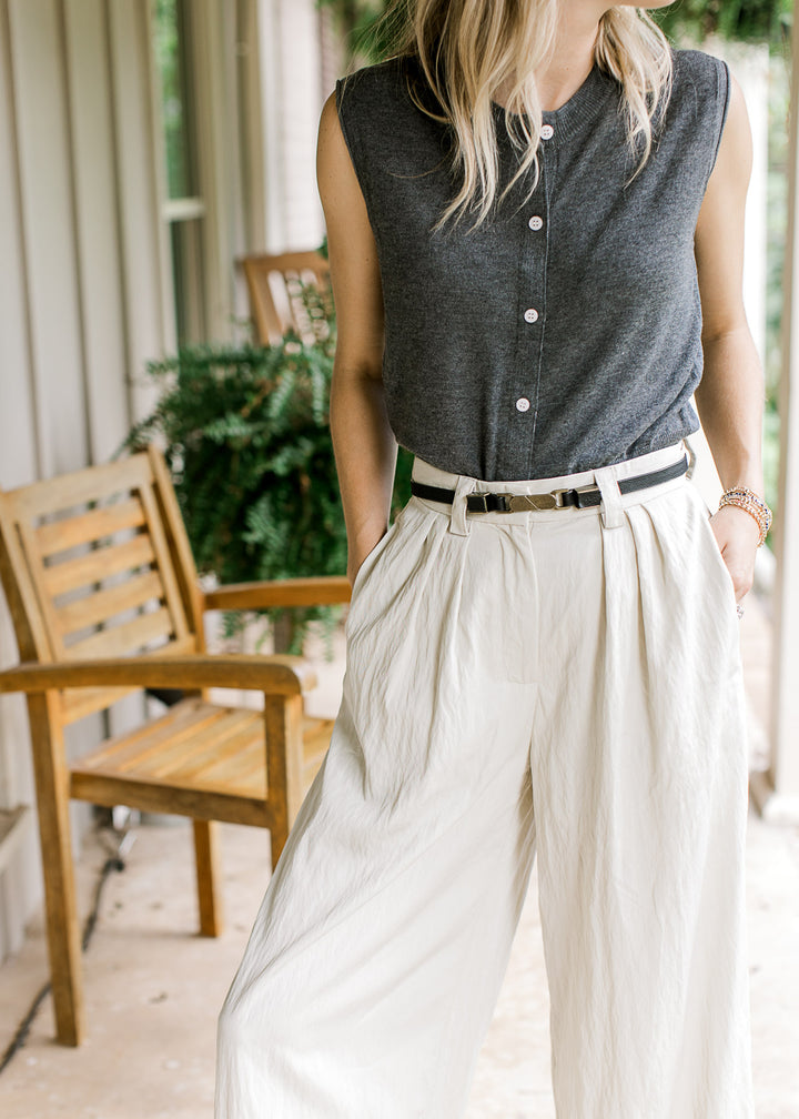 Model wearing creamy white wide leg pants with a pleated front and adjustable button closure. 