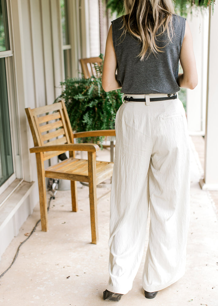 Back view of Model wearing cream wide leg pants with a pleated front and adjustable button closure. 
