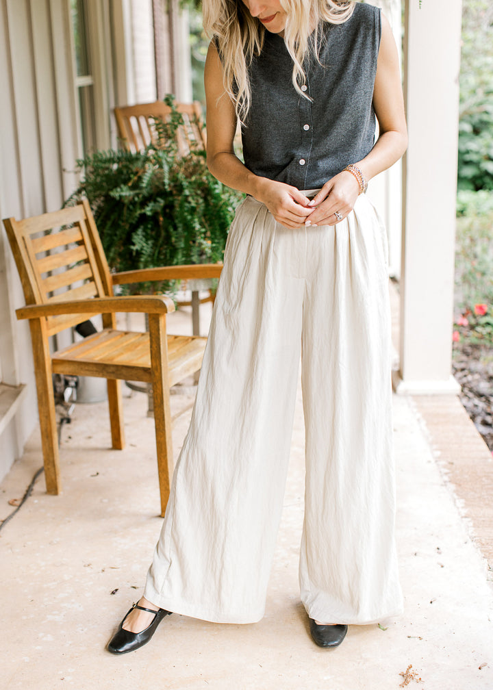 Model wearing a gray top and creamy white wide leg pants with a pleated front. 