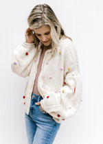 Model wearing an cozy oatmeal open front cardigan with bubble long sleeves and colored pop-poms. 