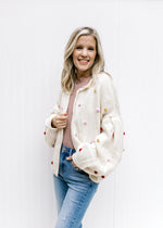 Side view of Model wearing an oatmeal cardigan with bubble long sleeves and colored pop-poms. 